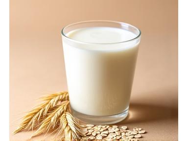 Susu oat berkrim dalam gelas dengan oat mentah di latar belakang.